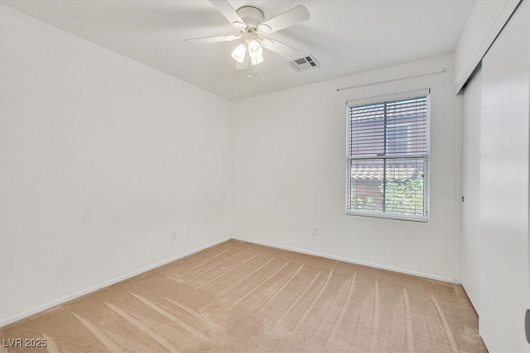 Empty bedroom with beige carpet, a white ceiling fan, and a window with blinds.