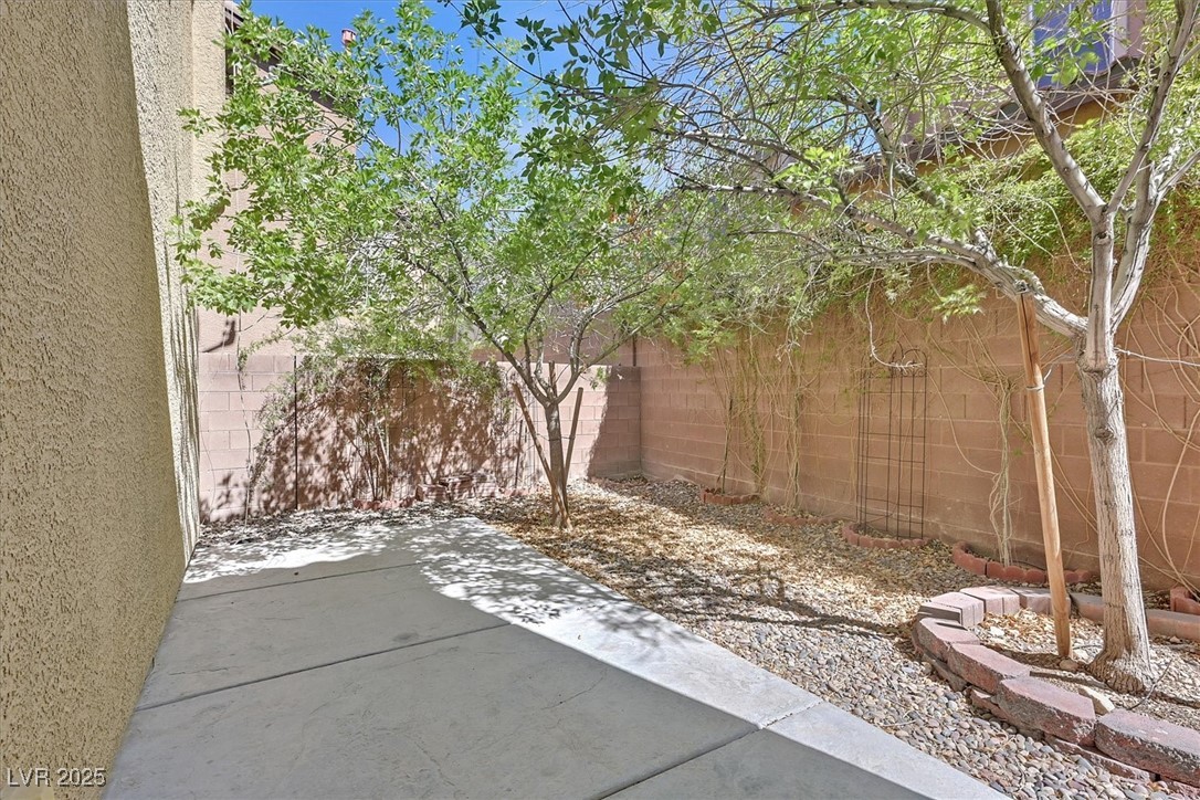 Backyard patio with a concrete slab, gravel landscaping, leafy trees, and tan block walls.