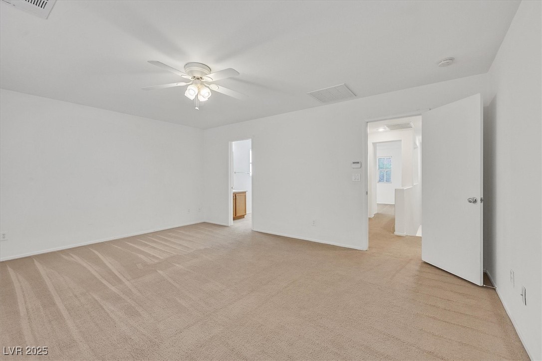 Empty carpeted bedroom with a ceiling fan and open doors to the hallway and bathroom.