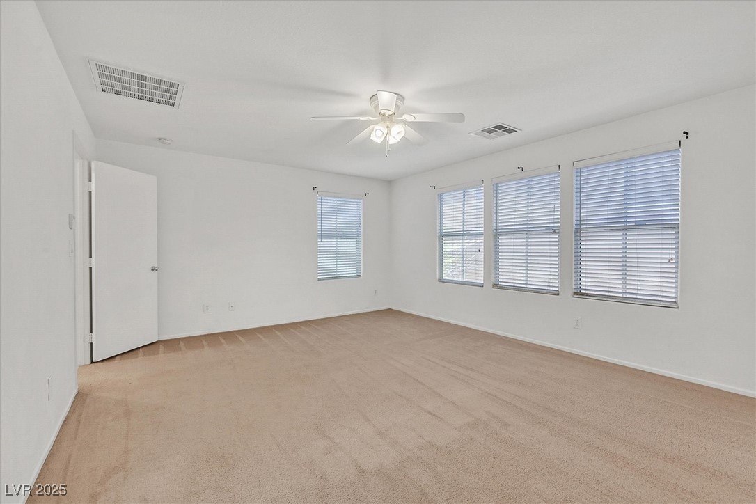 Empty carpeted room with four windows, blinds, and a ceiling fan.