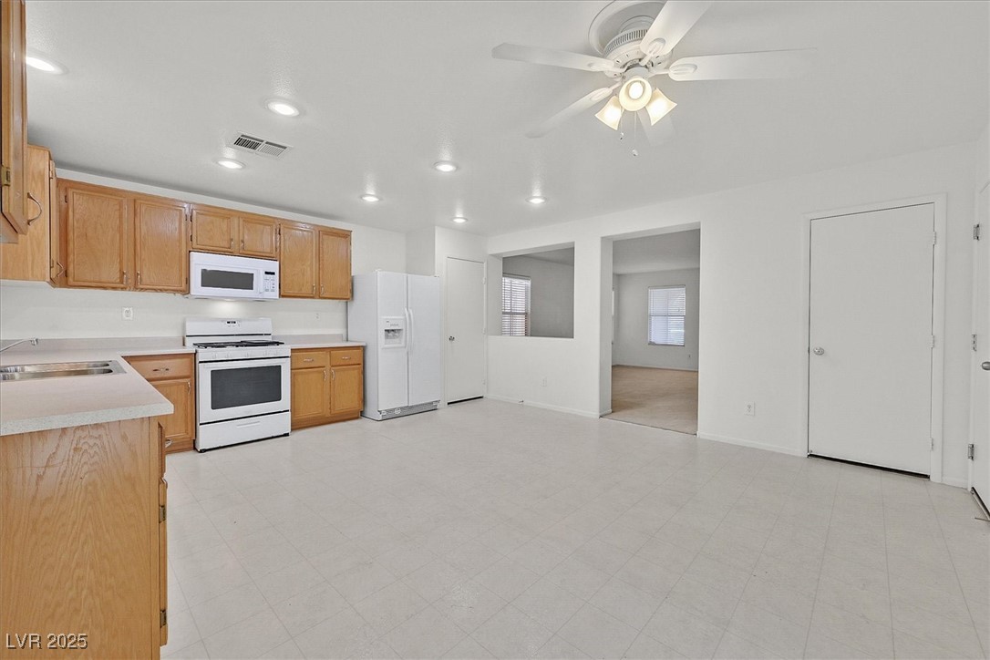 Vacant kitchen with light wood cabinets, white appliances, and open doorways to adjoining rooms.