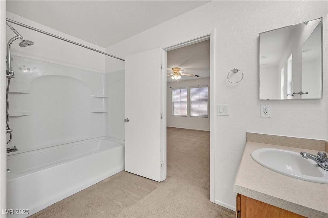 Bathroom with a white tub and shower, vanity, and doorway to a room with two windows.