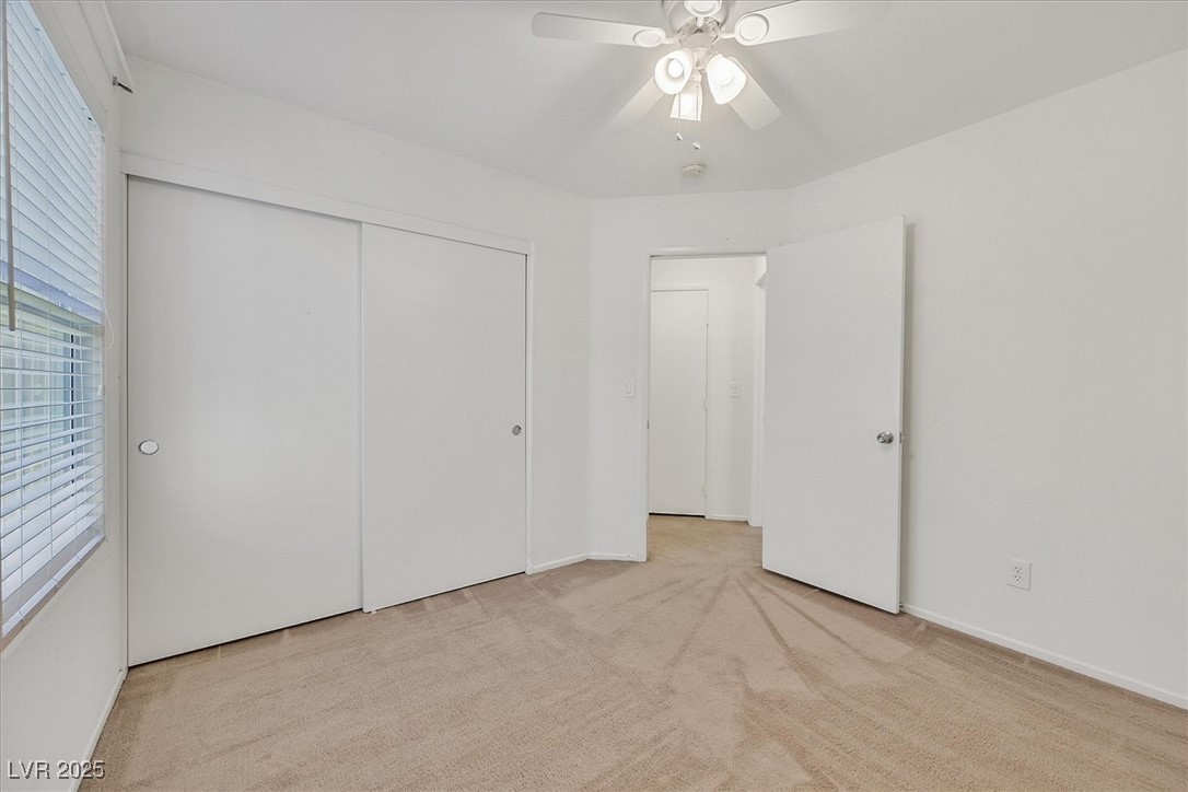 Empty bedroom with beige carpet, ceiling fan, window blinds, and sliding-door closet.