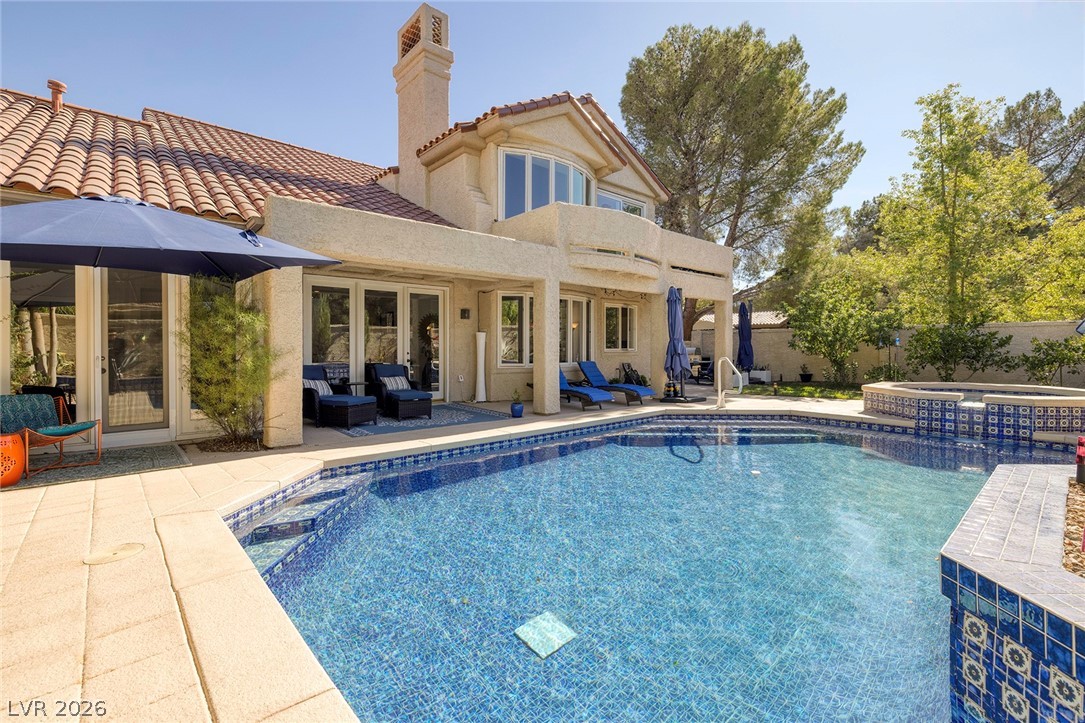 Backyard swimming pool with raised tiled spa, patio seating, and a two-story stucco home.