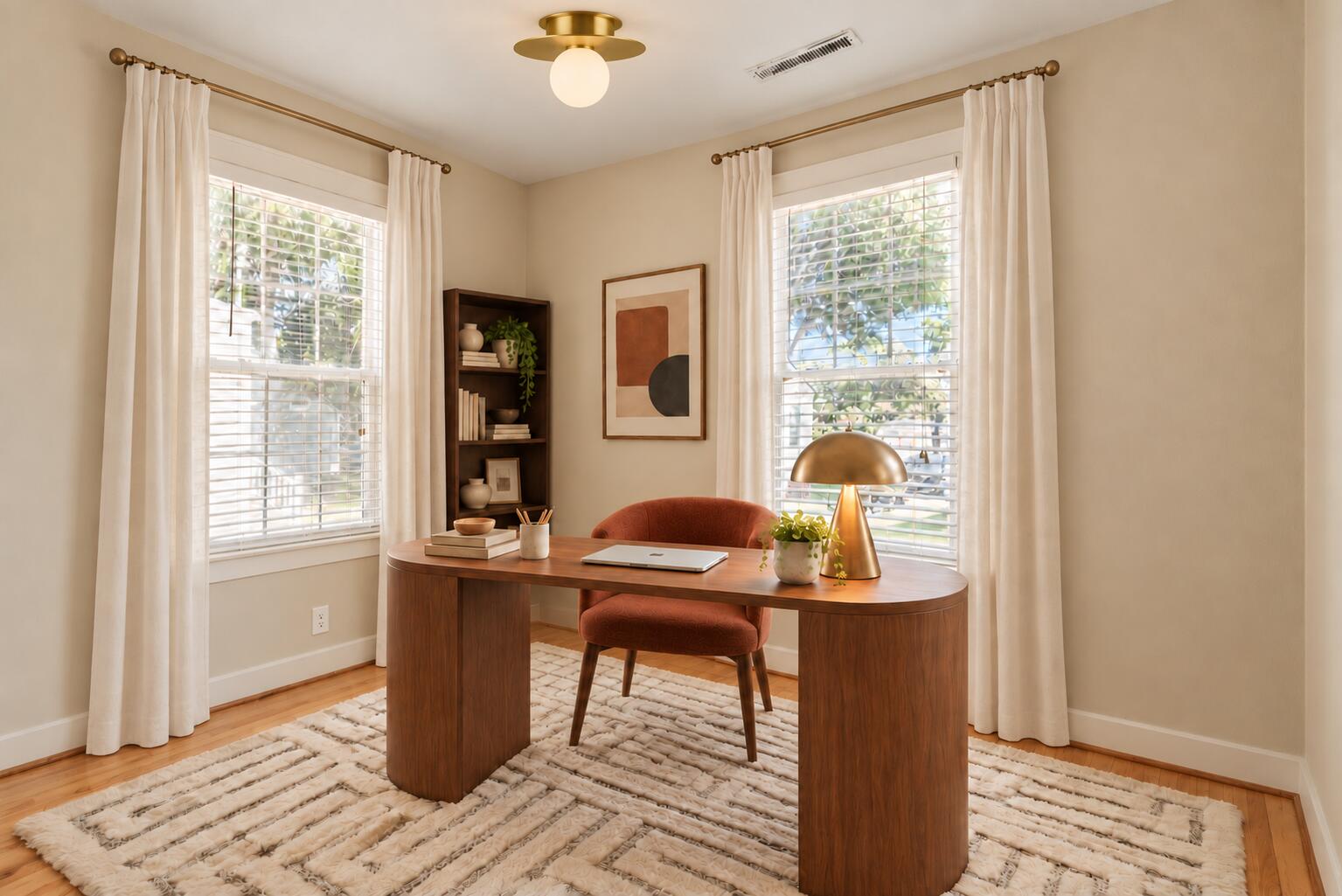 Staged home office with a curved walnut desk, rust-colored chair, and two large curtained windows.
