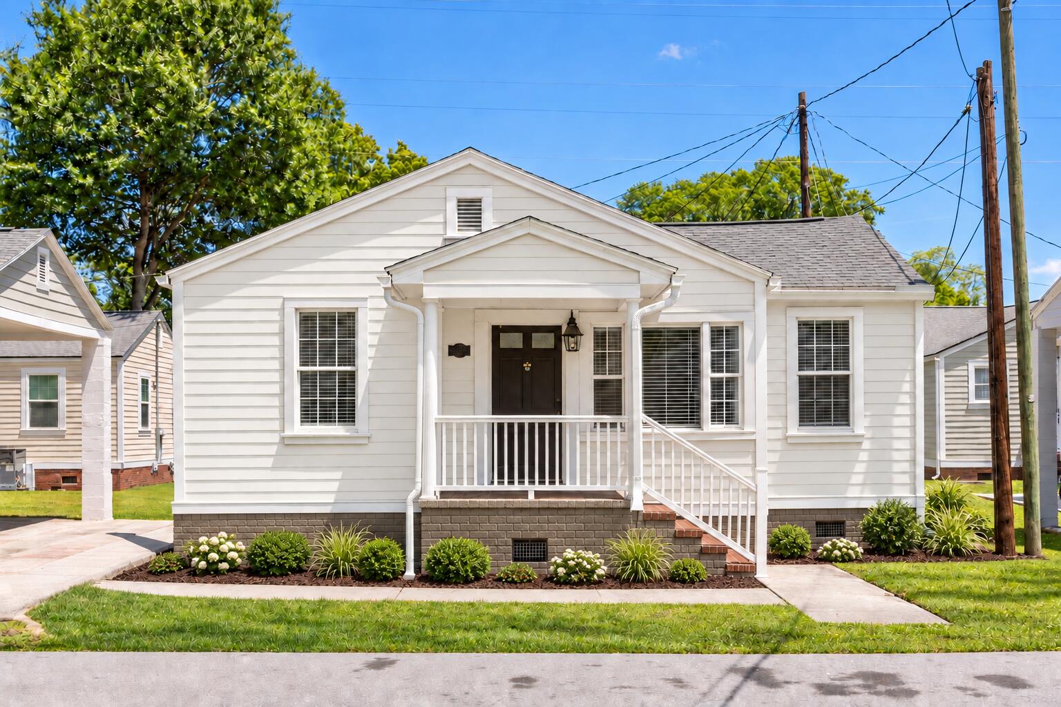White single-story house with a covered porch, brick steps, and landscaped front garden.