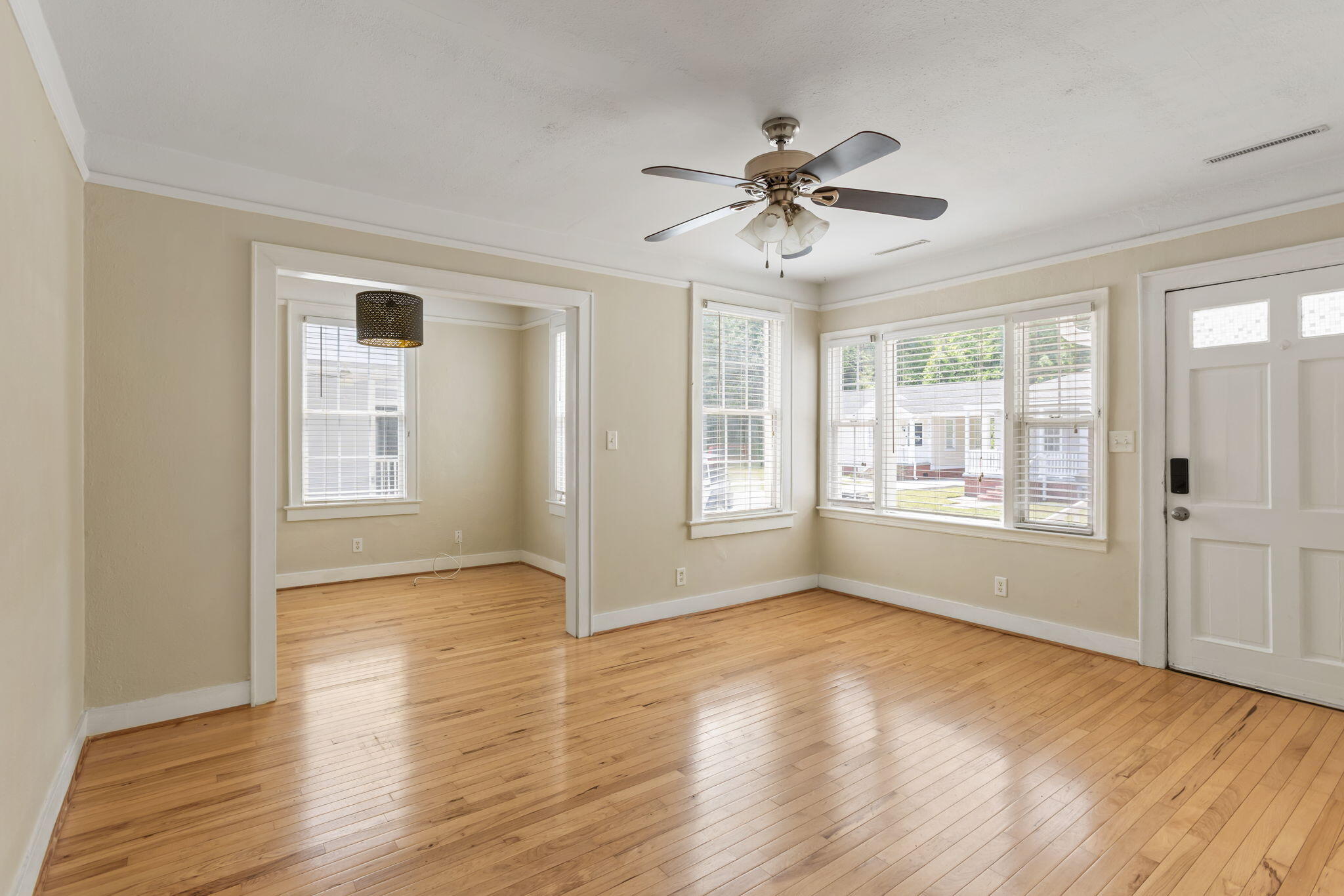 Vacant living room with hardwood floors, a ceiling fan, and a wide doorway to an adjoining room.