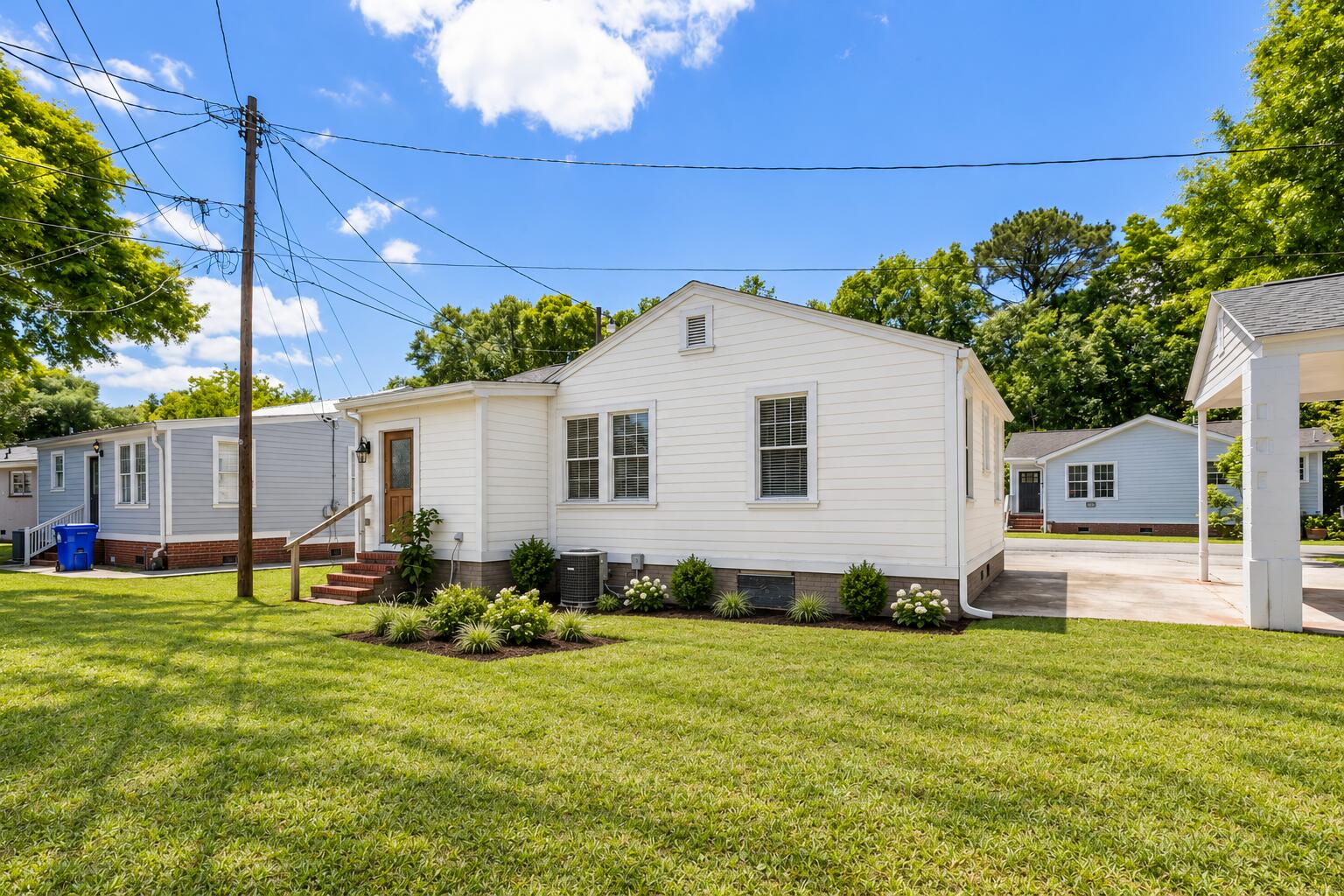 White single-story home with a small front stoop, landscaped foundation, and broad green lawn.