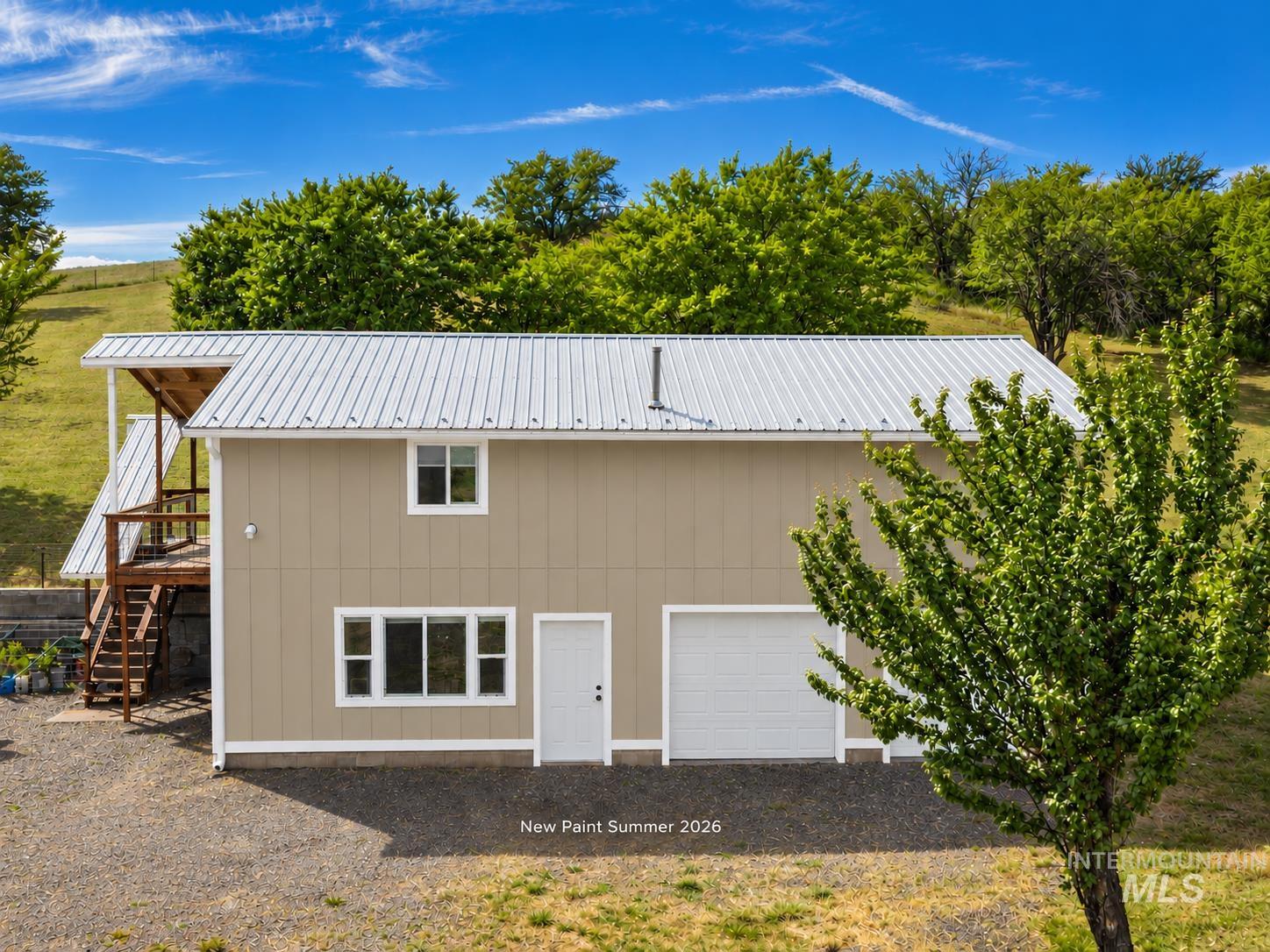 Tan home with a white metal roof, attached garage, and exterior stairs framed by trees.