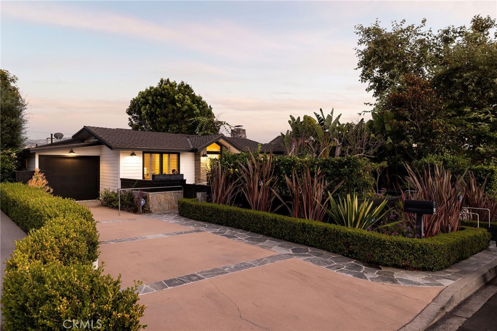 Single-story home with a landscaped front yard, stone-edged driveway, and illuminated windows at dusk.