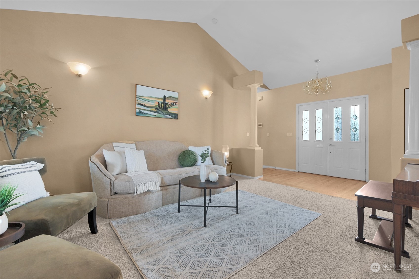 Staged living room with vaulted ceiling, patterned rug, and decorative-glass double entry doors.