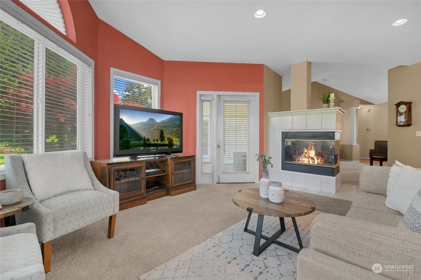 Furnished living room with a tiled fireplace, red accent wall, large windows, and neutral seating.