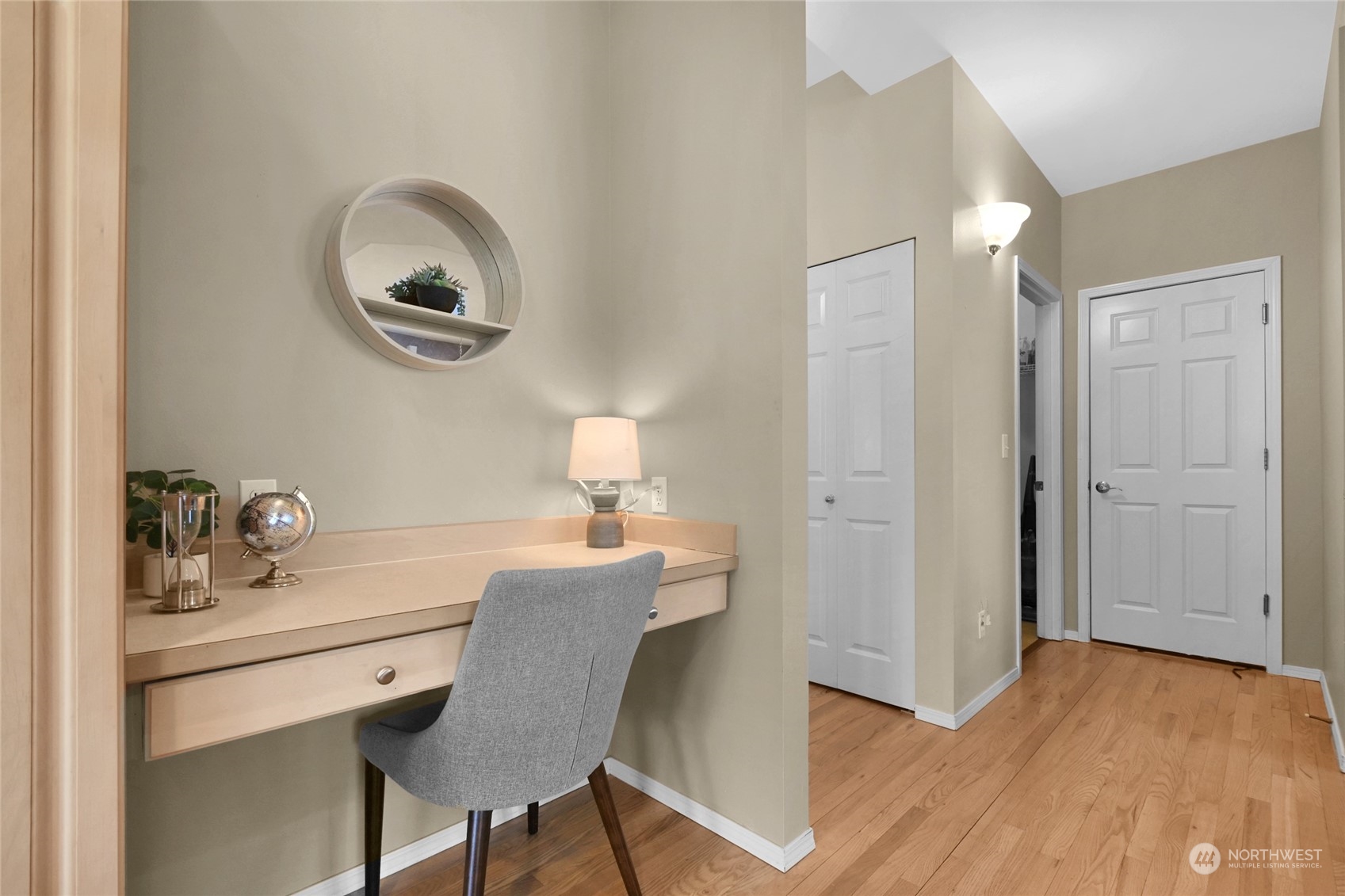 Staged home office nook with built-in desk and gray chair beside a hardwood-floored entry hall.