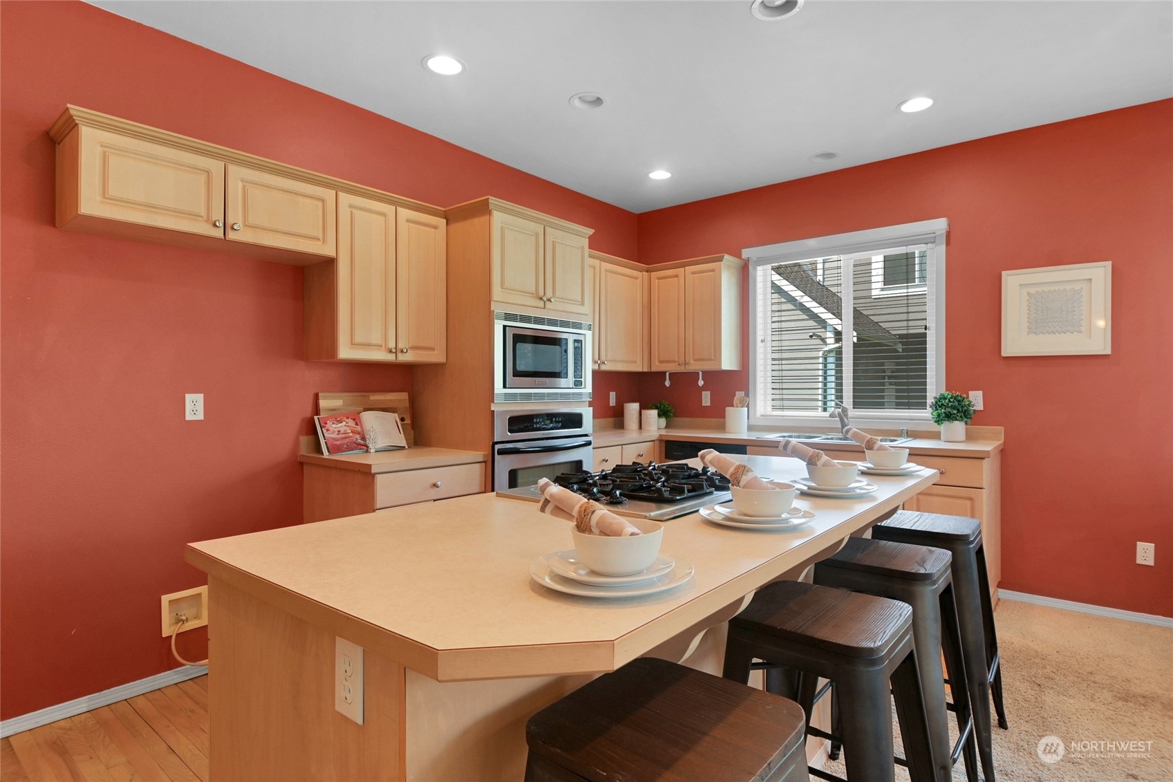 Kitchen with a large cooktop island, light wood cabinetry, and coral-red walls.