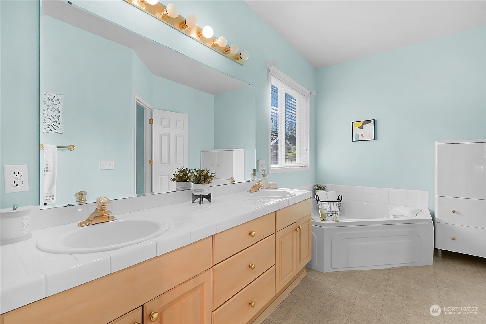 Bathroom with a long double-sink vanity, light wood cabinets, and a built-in bathtub beneath a window.