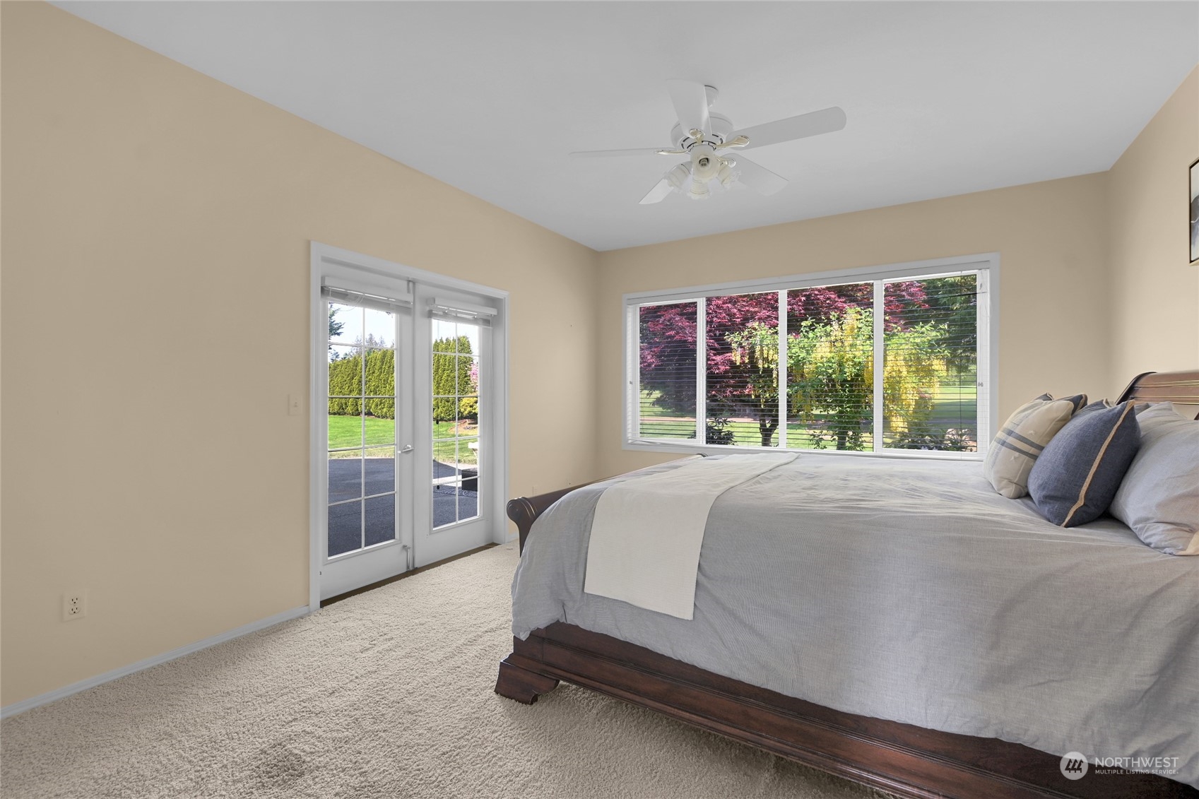 Staged bedroom with a dark wood bed and French doors opening toward a landscaped yard.
