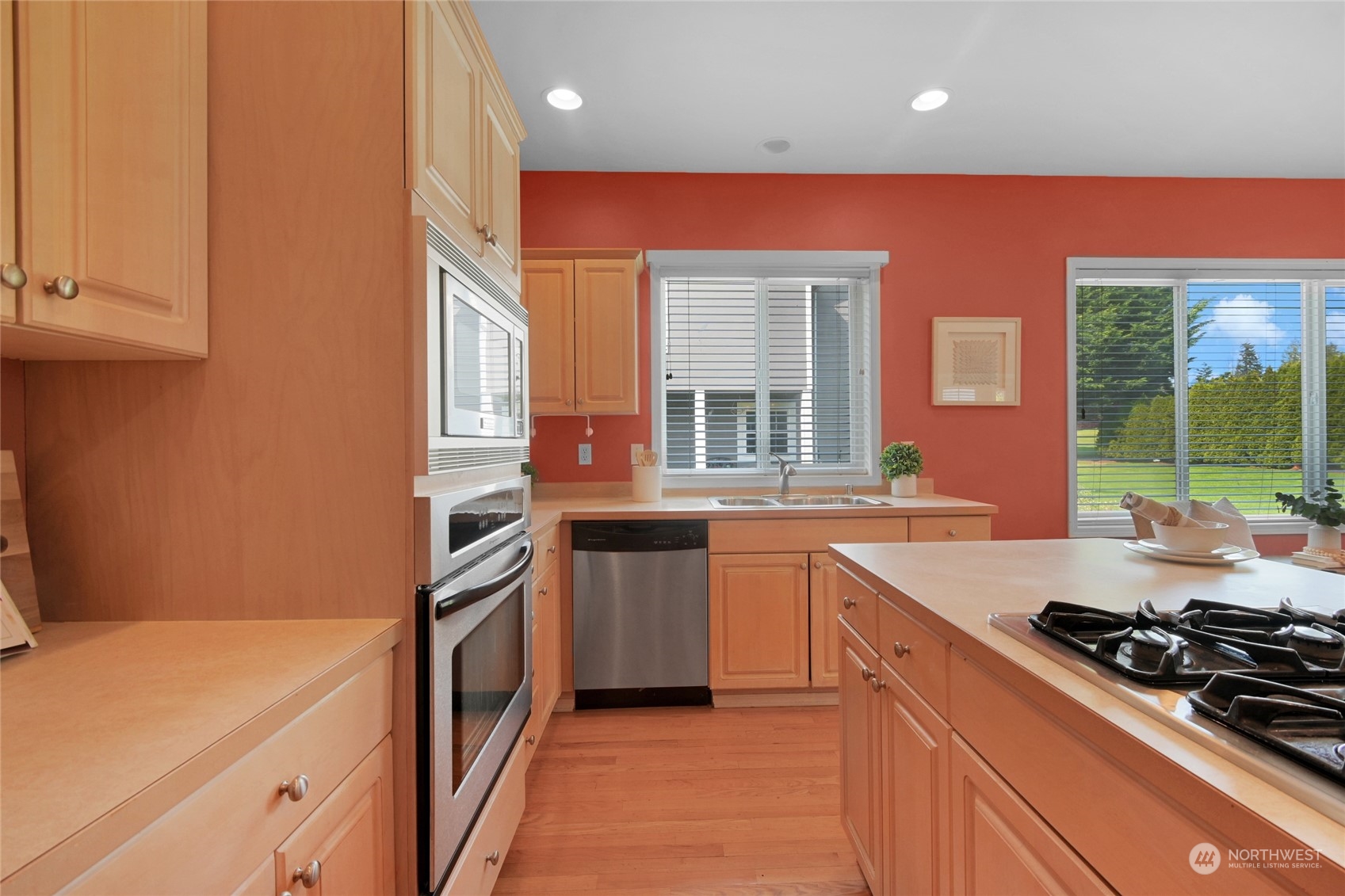 Kitchen with warm wood cabinets, hardwood floors, a gas cooktop island, and windows overlooking greenery.