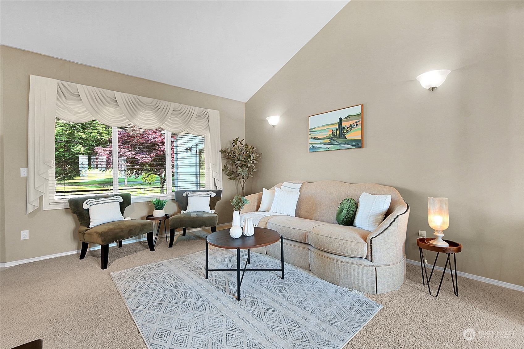 Living room with a beige sofa, two accent chairs, and a large window overlooking flowering trees.
