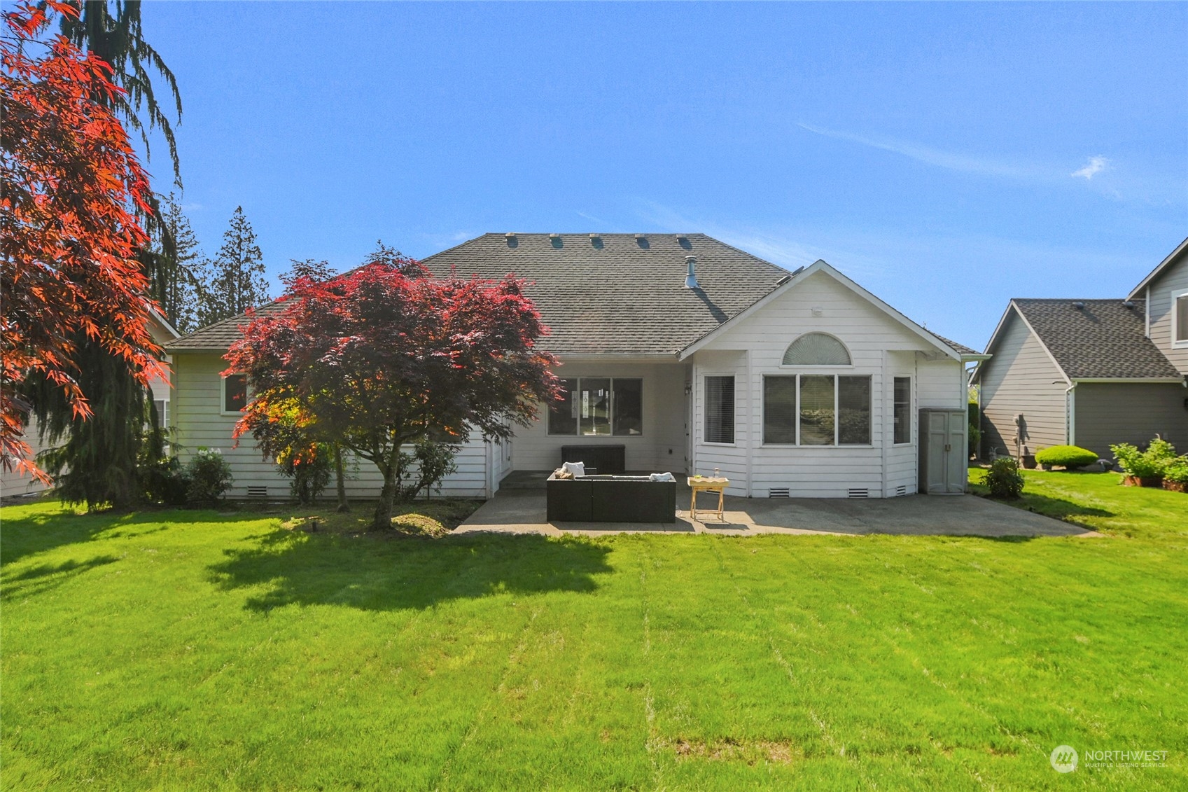 Rear of a white single-story home with a covered patio, outdoor seating, and a broad green lawn.