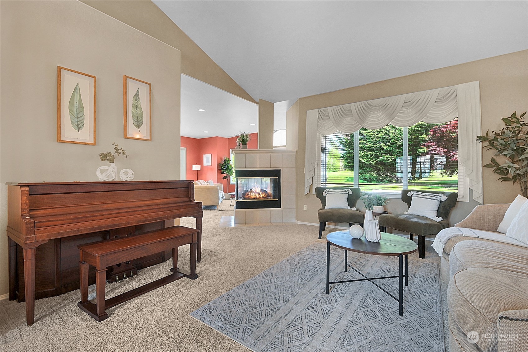 Living room with a dark wood piano, lit fireplace, and large window overlooking a green yard.