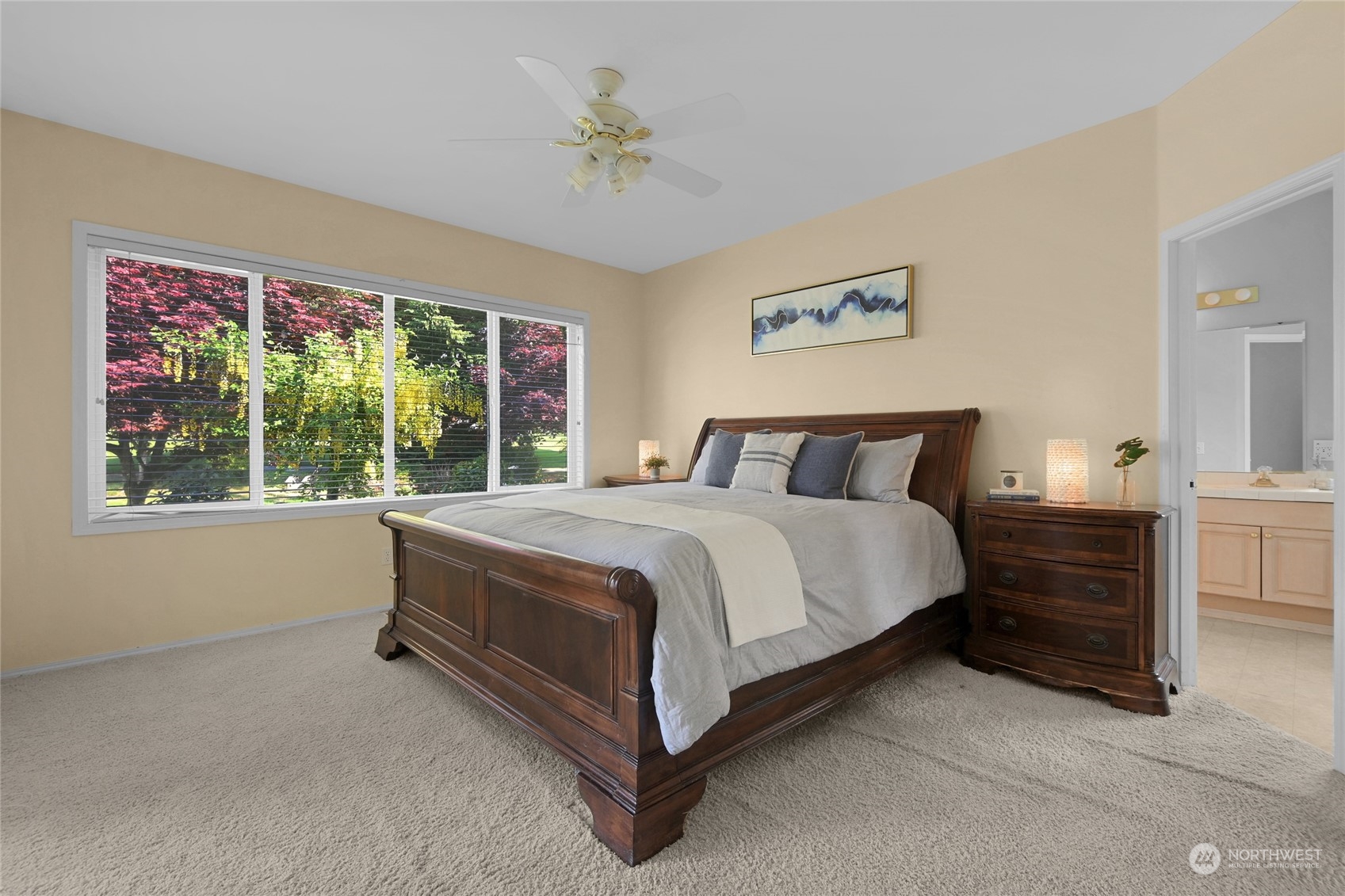 Furnished bedroom with a dark wood bed, wide garden-facing window, and doorway to an ensuite bathroom.