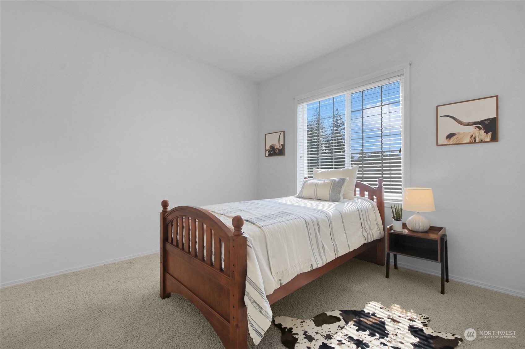 Bright bedroom with a wooden bed, striped white bedding, and a large window with blinds.