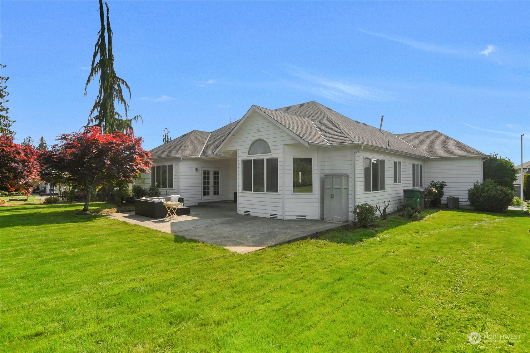 White single-story house with a concrete patio, outdoor seating, and broad green lawn.