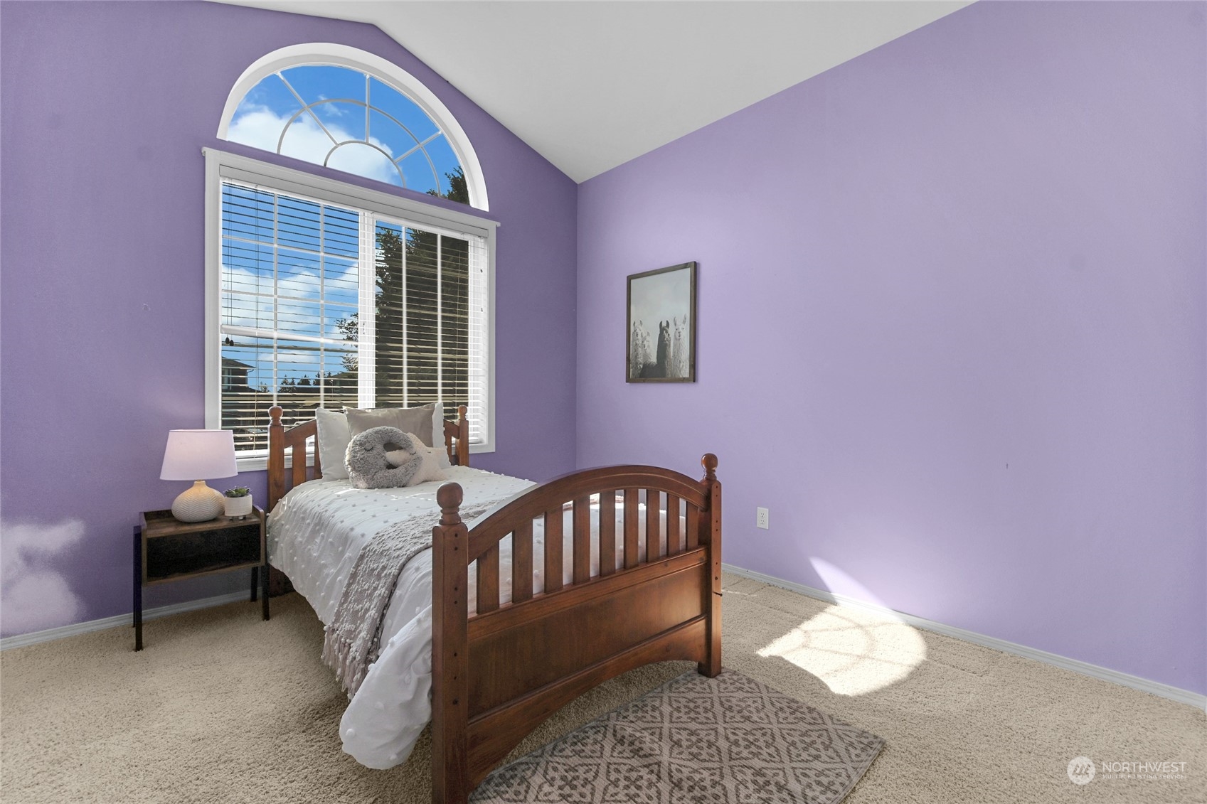 Bedroom with lavender walls, a wooden twin bed, and a large arched window.