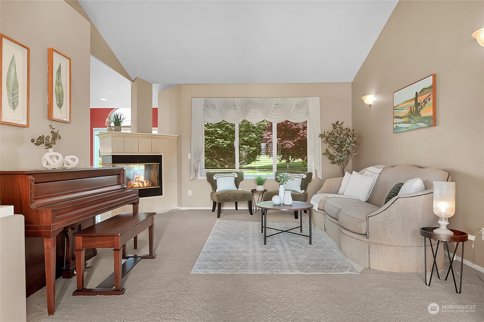 Living room with a tiled fireplace, upright piano, and large window overlooking trees.