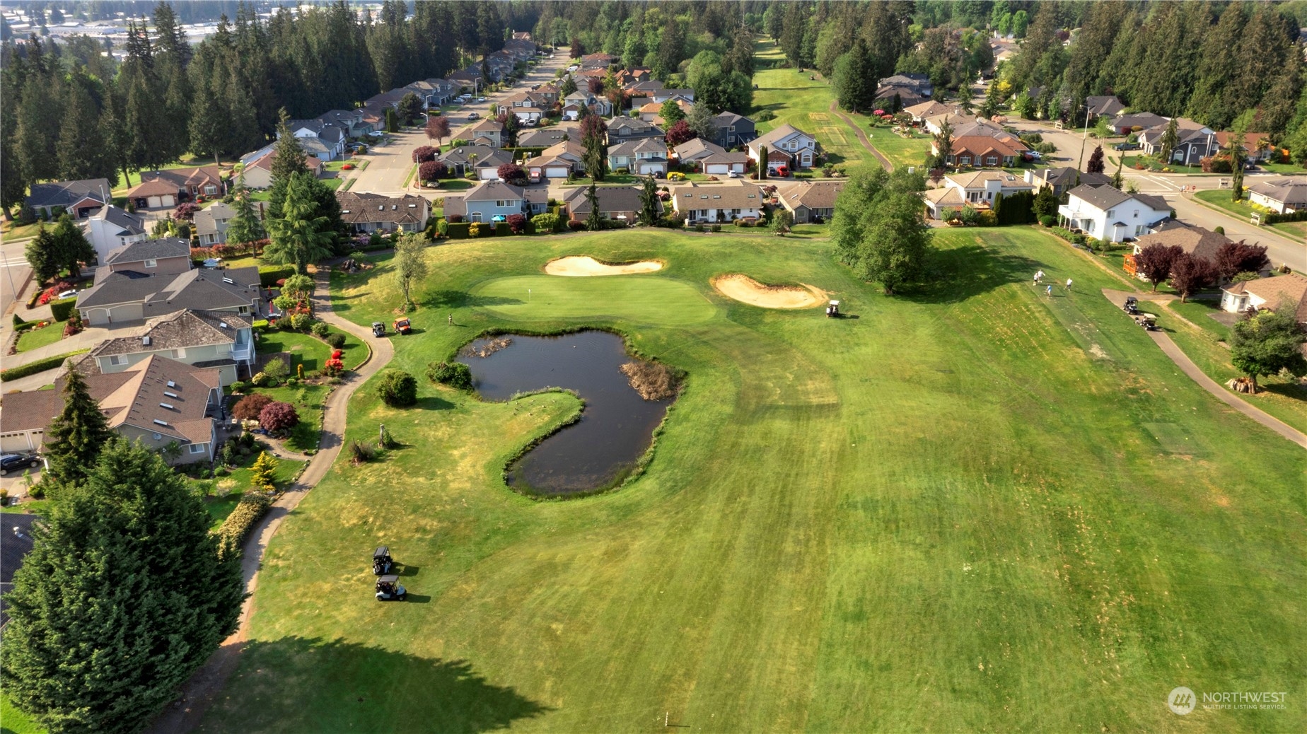 Aerial view of a neighborhood golf course with a winding pond and sand bunkers.