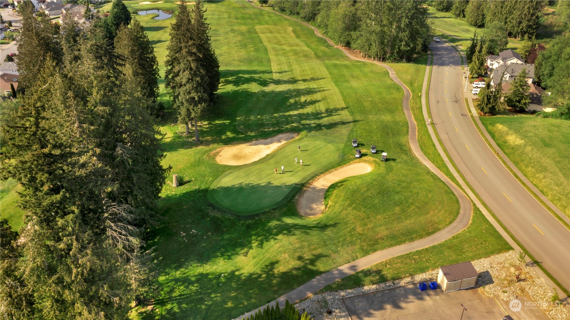 Aerial view of a golf course with sand traps and golfers beside a residential road.