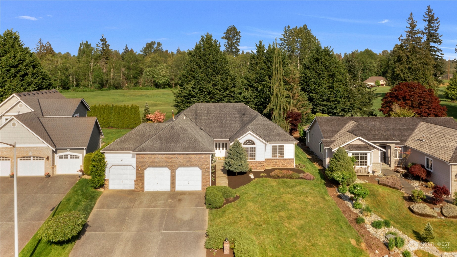 Aerial view of a brick-and-siding home with a three-car garage and landscaped front lawn.