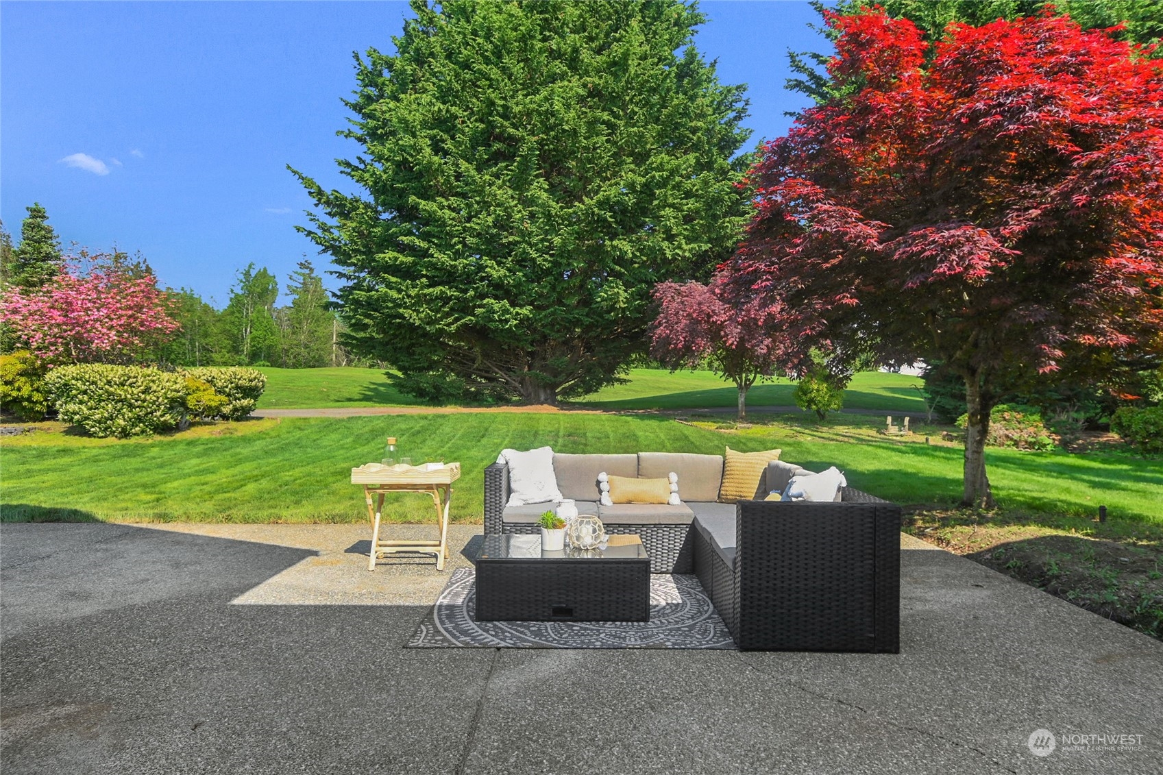 Furnished patio with wicker seating overlooking a landscaped lawn and mature trees.