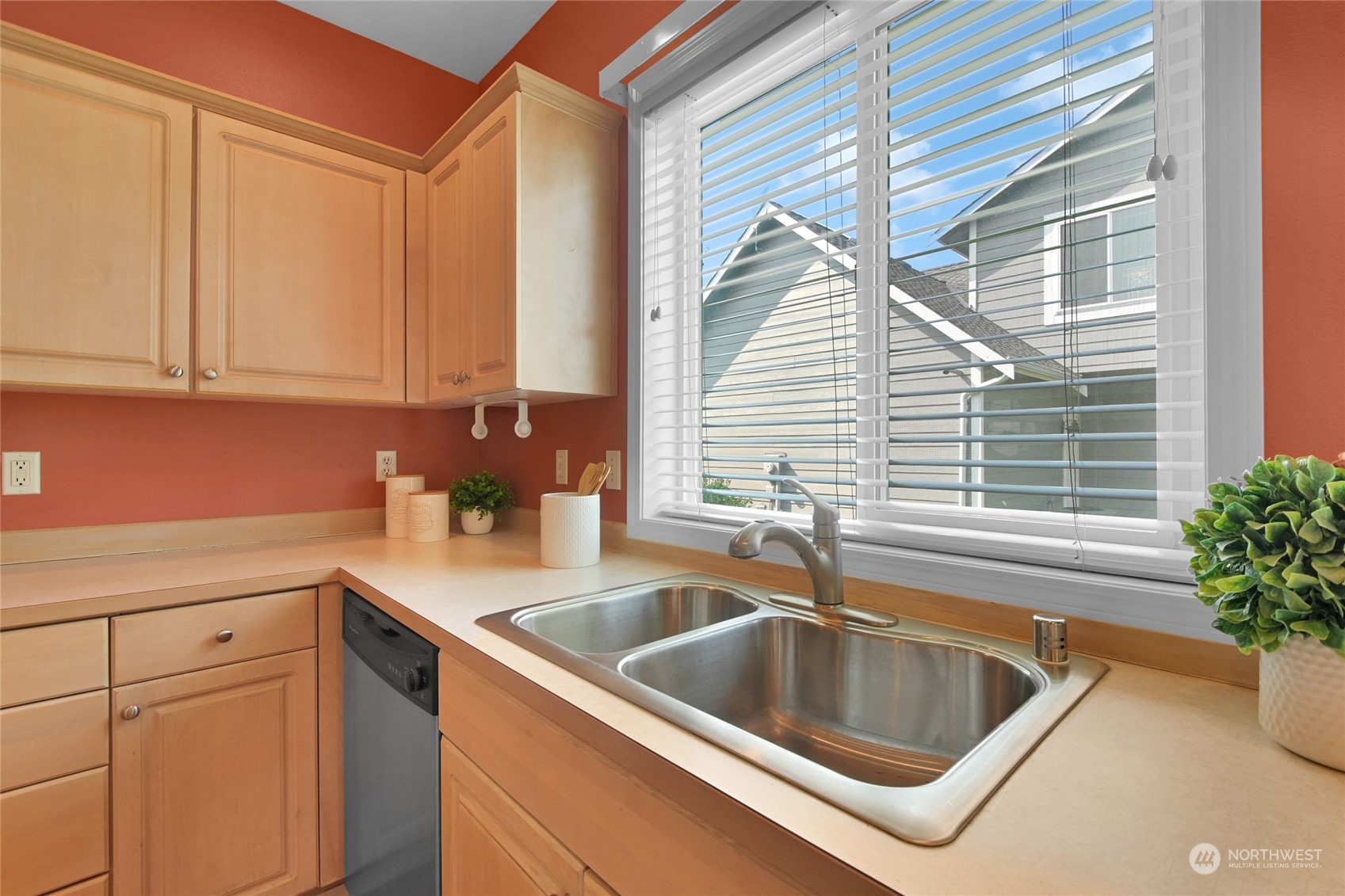Kitchen with a stainless-steel double sink beneath a large window, light wood cabinets, and terracotta walls.
