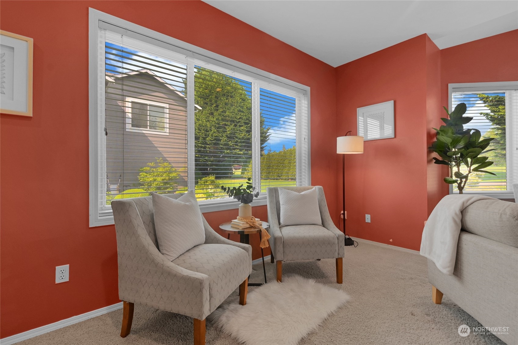 Living room sitting area with coral walls, upholstered armchairs, and large windows overlooking a green yard.