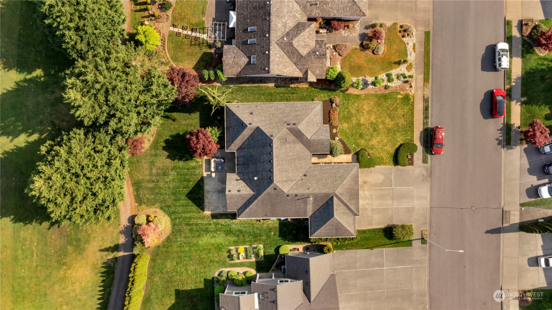 Aerial view of a gray-roofed home with landscaped lawns and neighboring houses along the street.