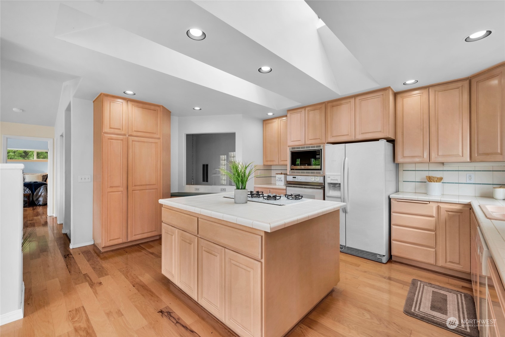 Kitchen with a large tiled island, gas cooktop, wood cabinetry, and hardwood floors.