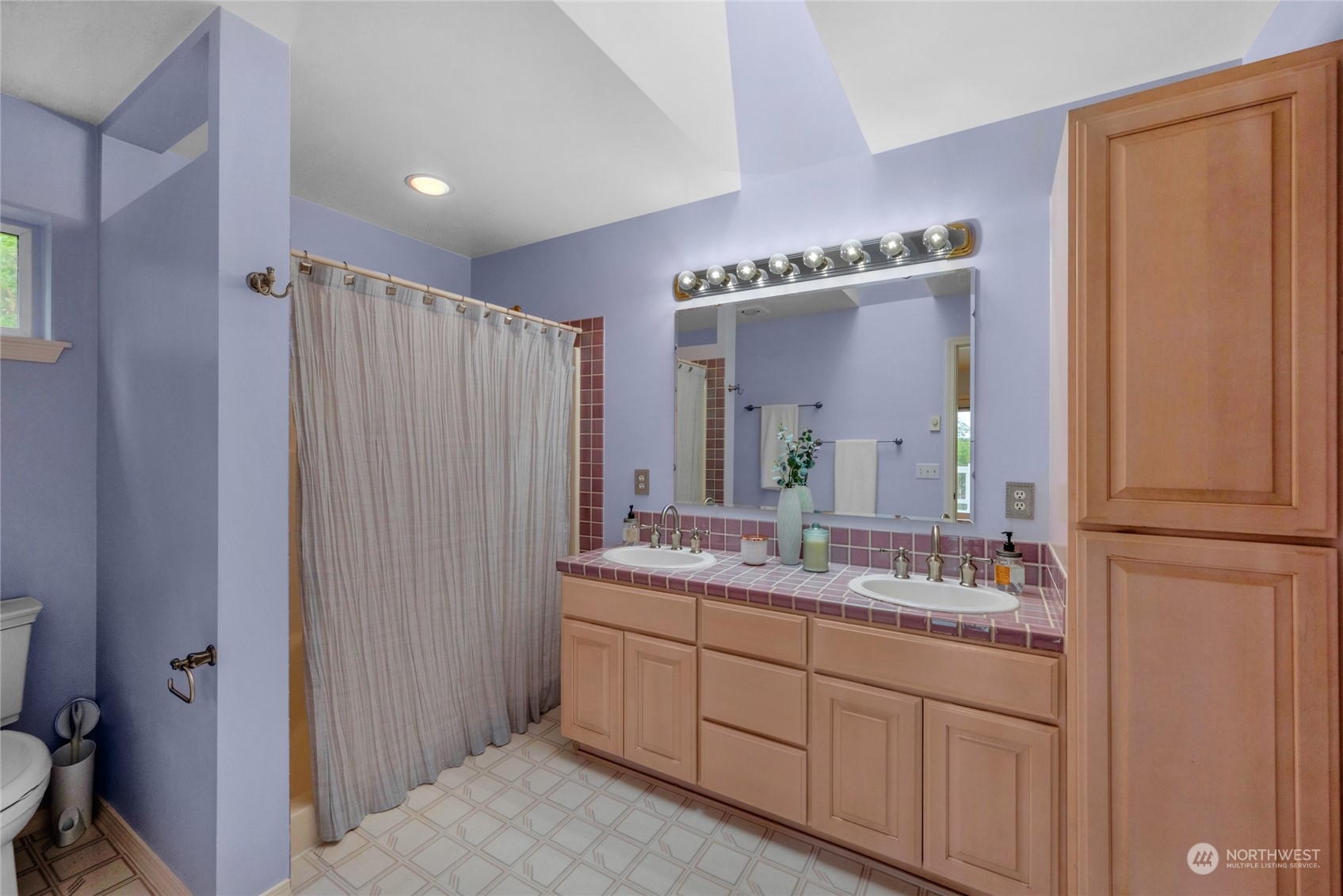 Bathroom with a double-sink vanity, pink tile countertop, wood cabinetry, and a curtained shower.