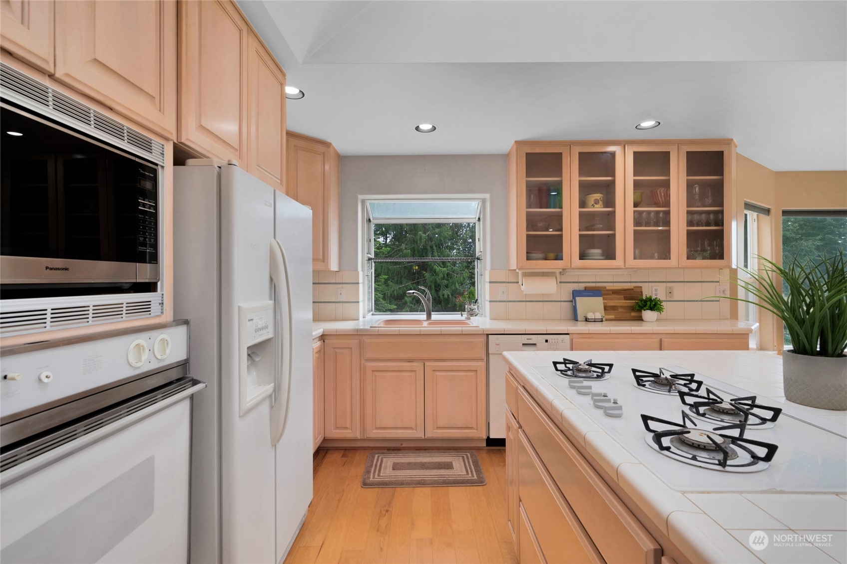 Kitchen with peach-toned cabinets, glass-front cupboards, and a large gas cooktop island.