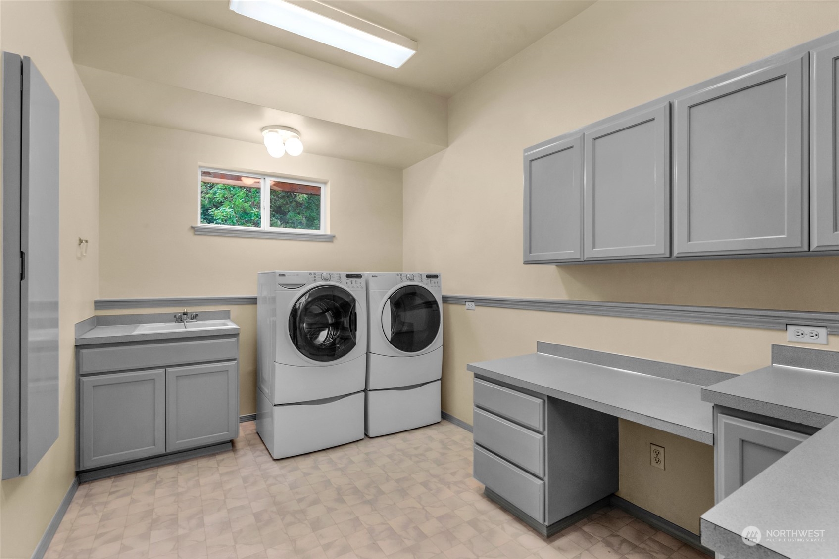Laundry room with front-loading washer and dryer, gray cabinetry, utility sink, and work counters.