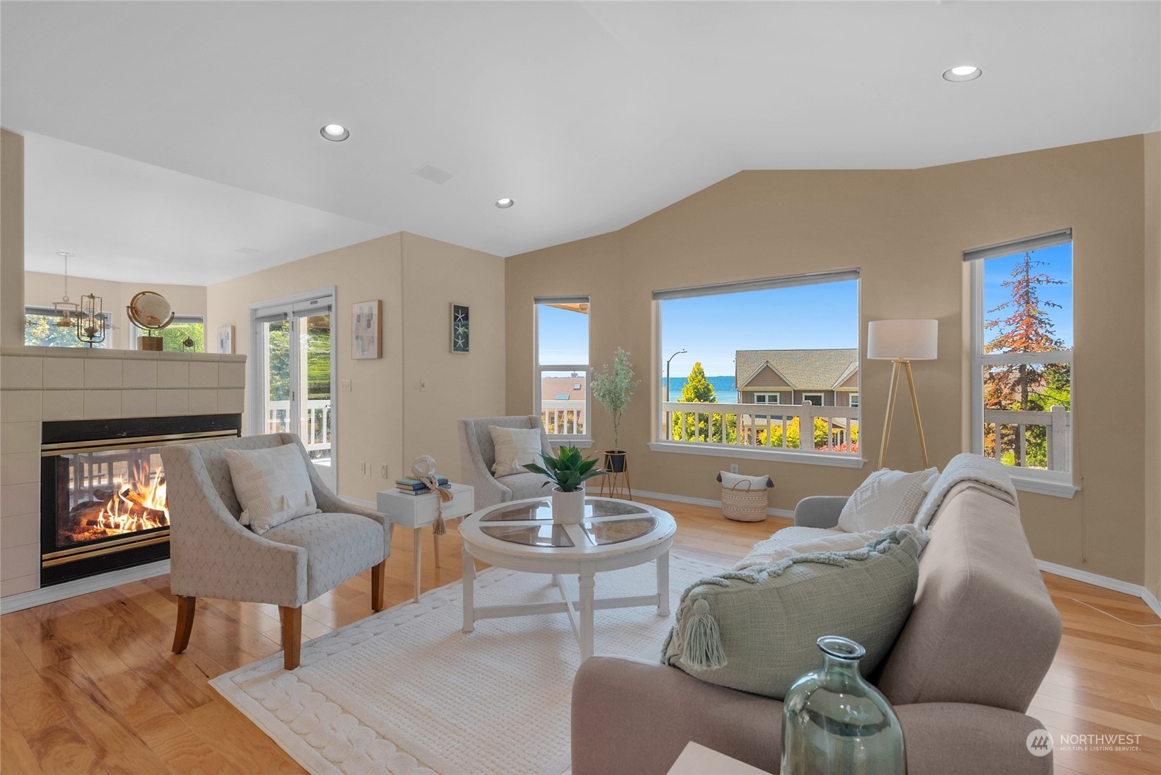 Staged living room with a lit fireplace and water views through large windows.