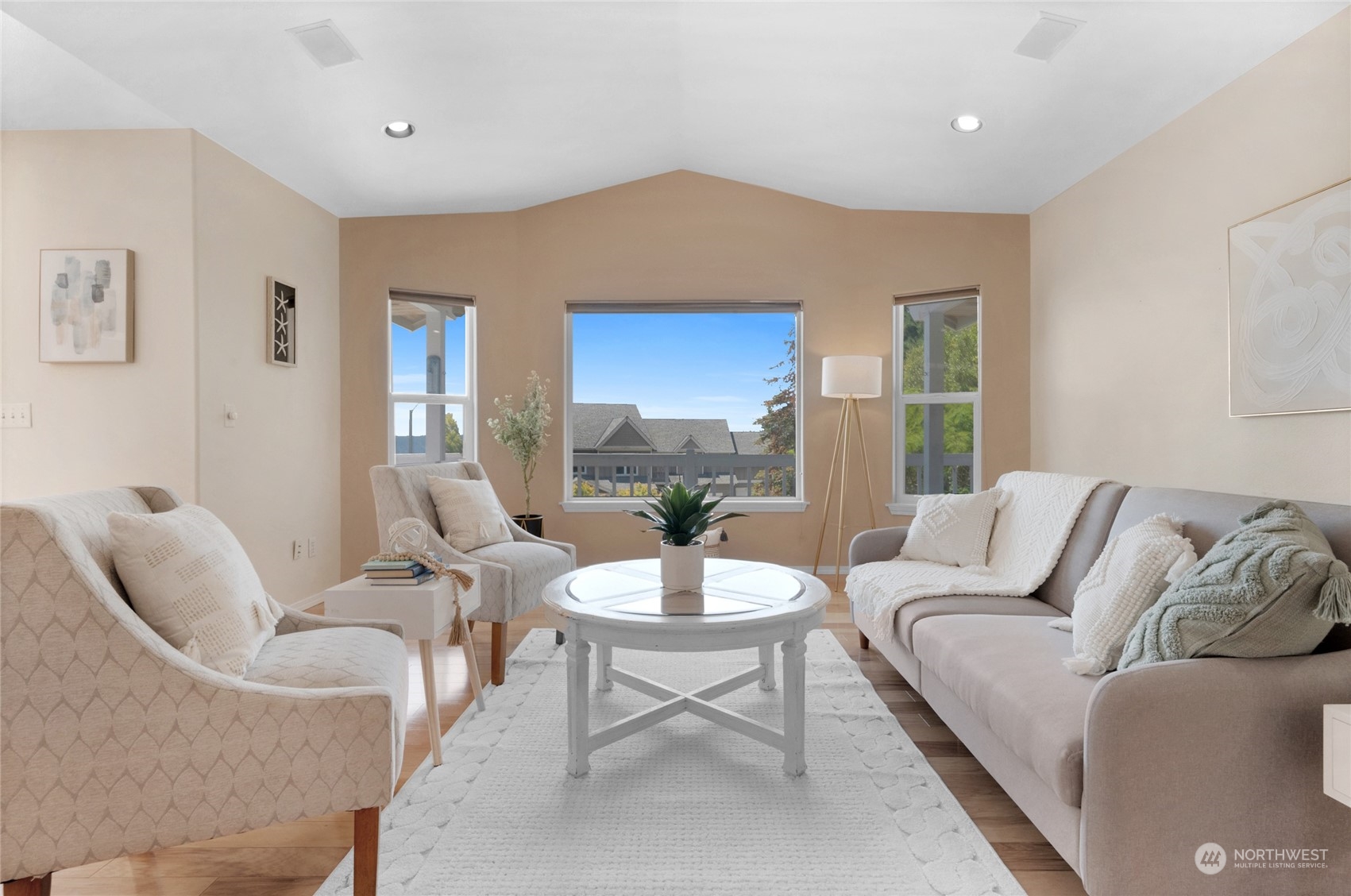 Furnished living room with neutral seating, a round coffee table, and three large windows.
