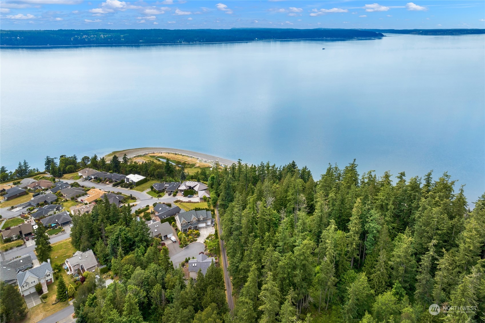 Aerial view of waterfront homes, a wooded shoreline, and broad calm water.