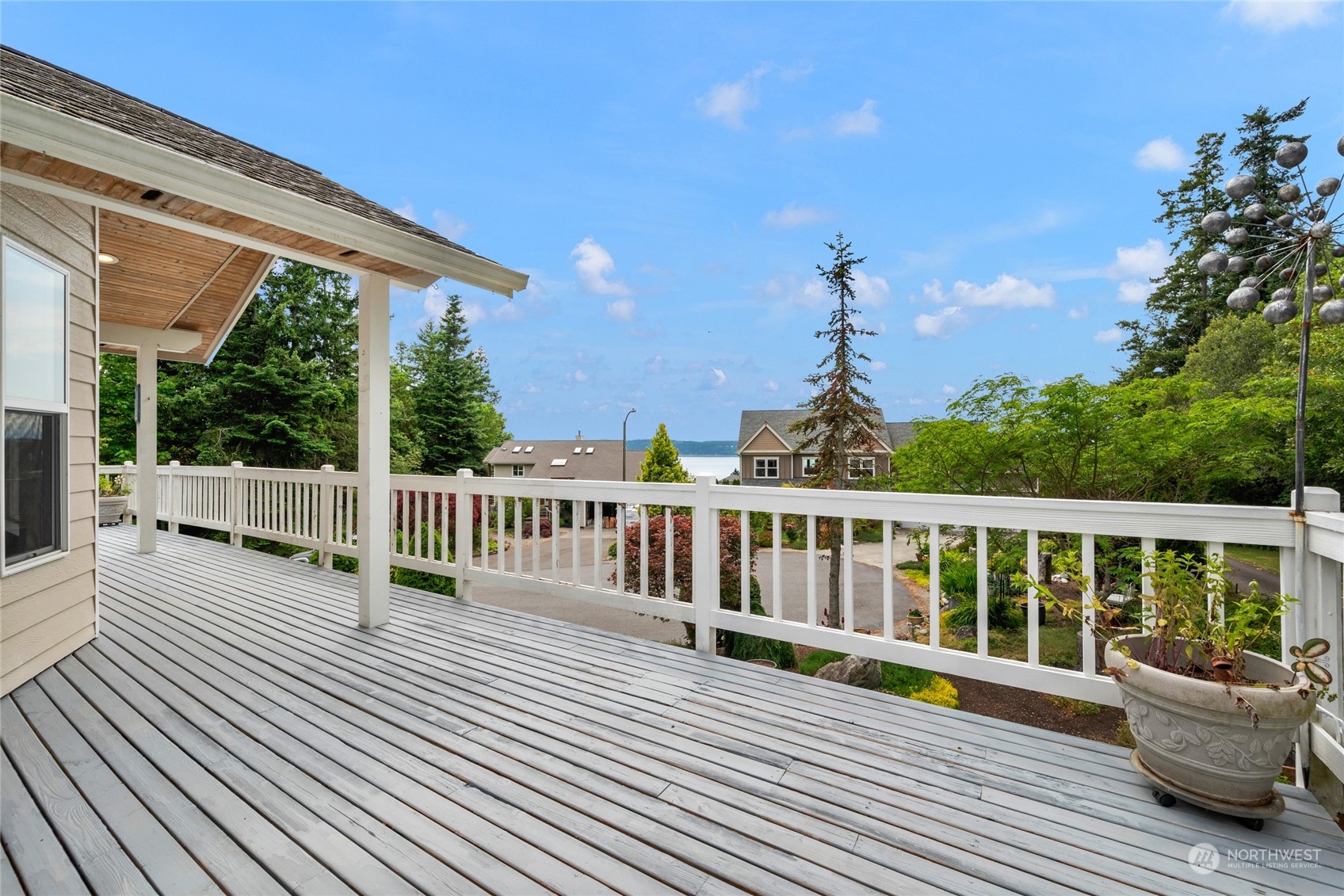Weathered deck with white railings overlooks neighboring homes, trees, and a narrow view of water.