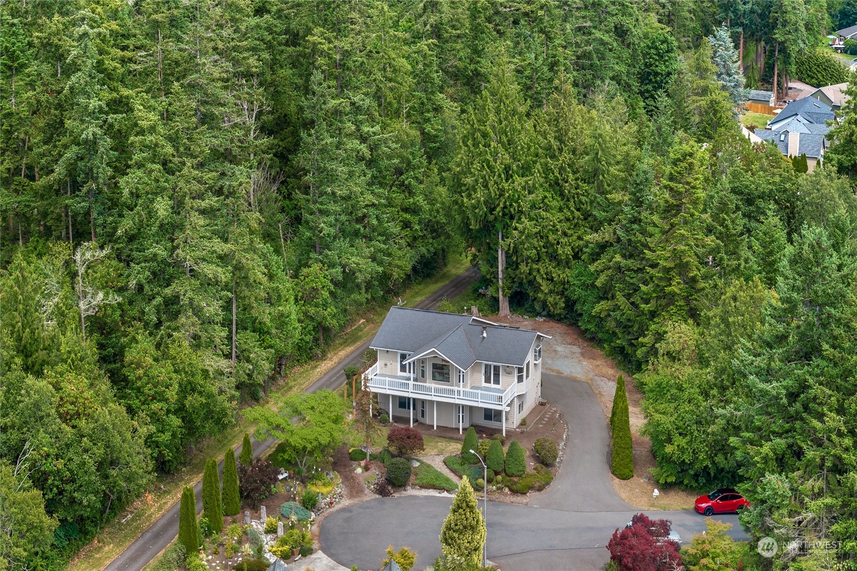 Aerial view of a two-story home and landscaped grounds surrounded by dense evergreen forest.