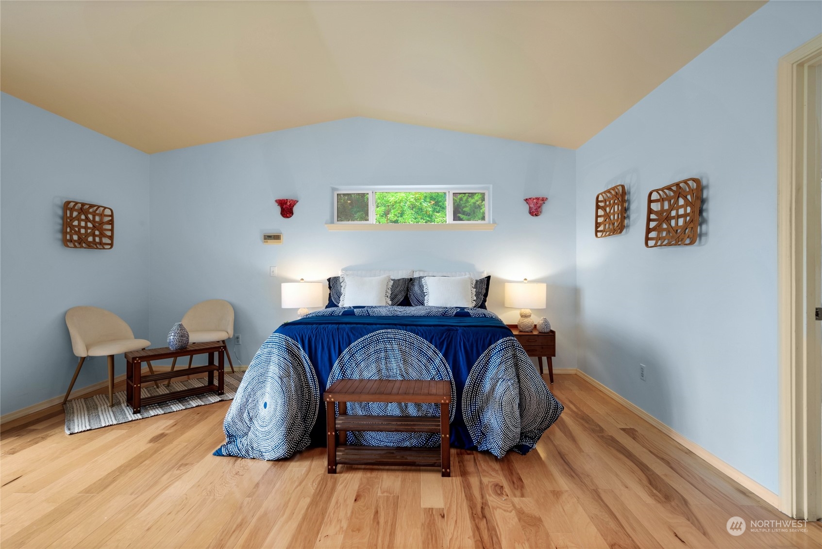 Staged bedroom with a king bed, navy patterned bedding, pale blue walls, and hardwood floors.