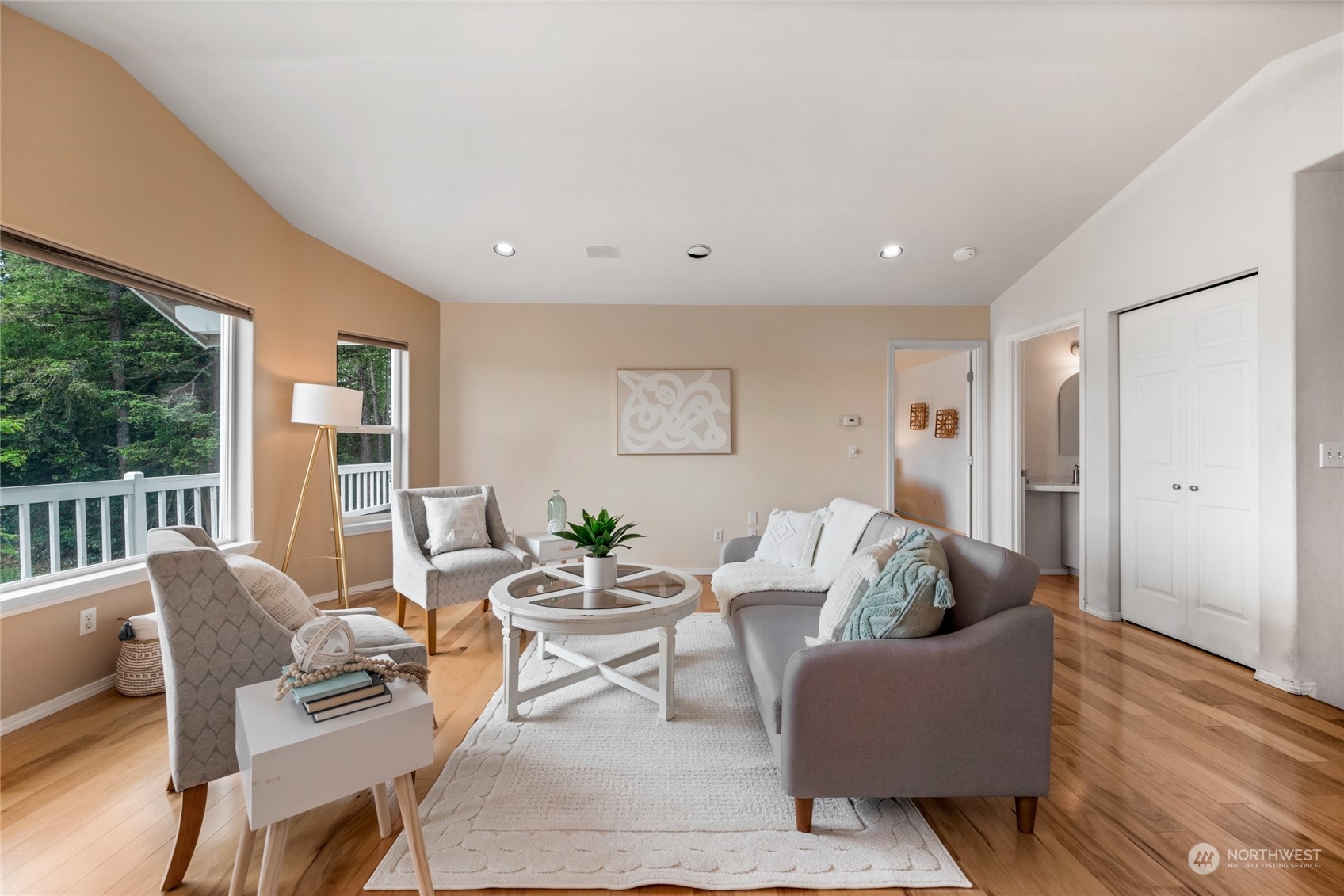 Living room with a gray sofa, hardwood floors, and large windows overlooking trees.
