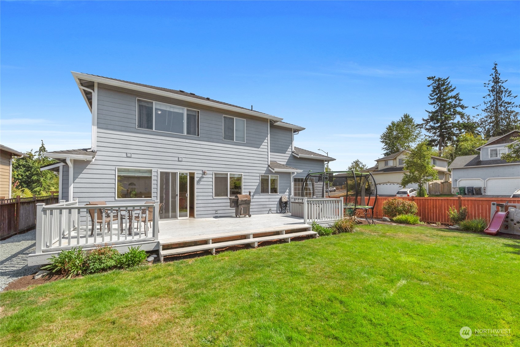 Gray two-story home with a white-railed deck, patio furniture, and a swing set in the grassy backyard.
