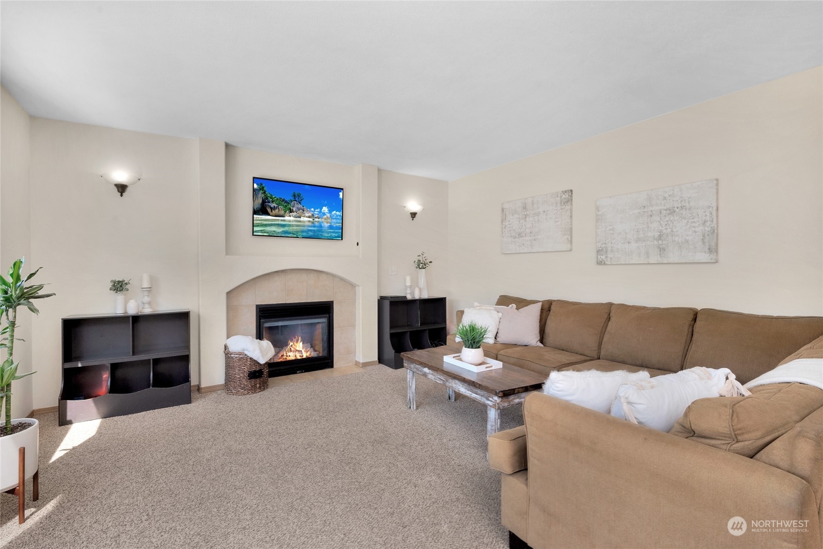 Living room with a beige sectional sofa and a lit fireplace beneath a wall-mounted television.