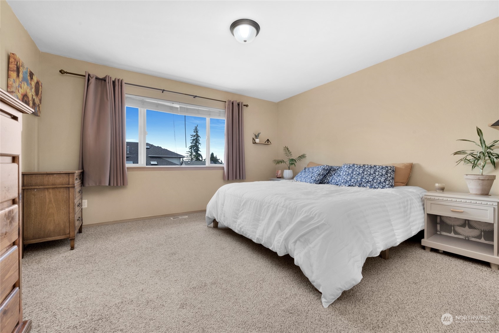 Bedroom with a large bed, carpet, and a wide window framed by mauve curtains.